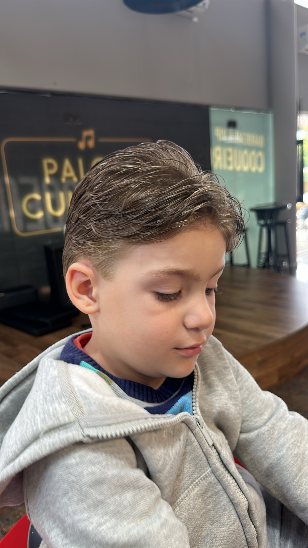 Corte infantil com topo penteado para trás e laterais raspadas, visto de frente