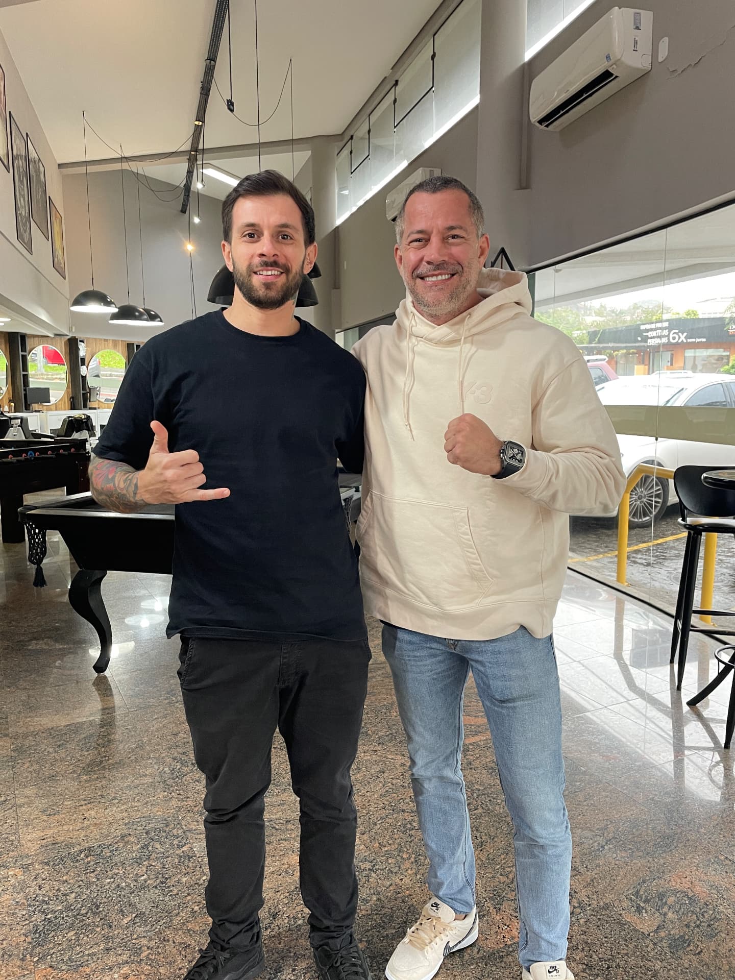 Murilo Oliveira ao lado de cliente atendido na barbearia