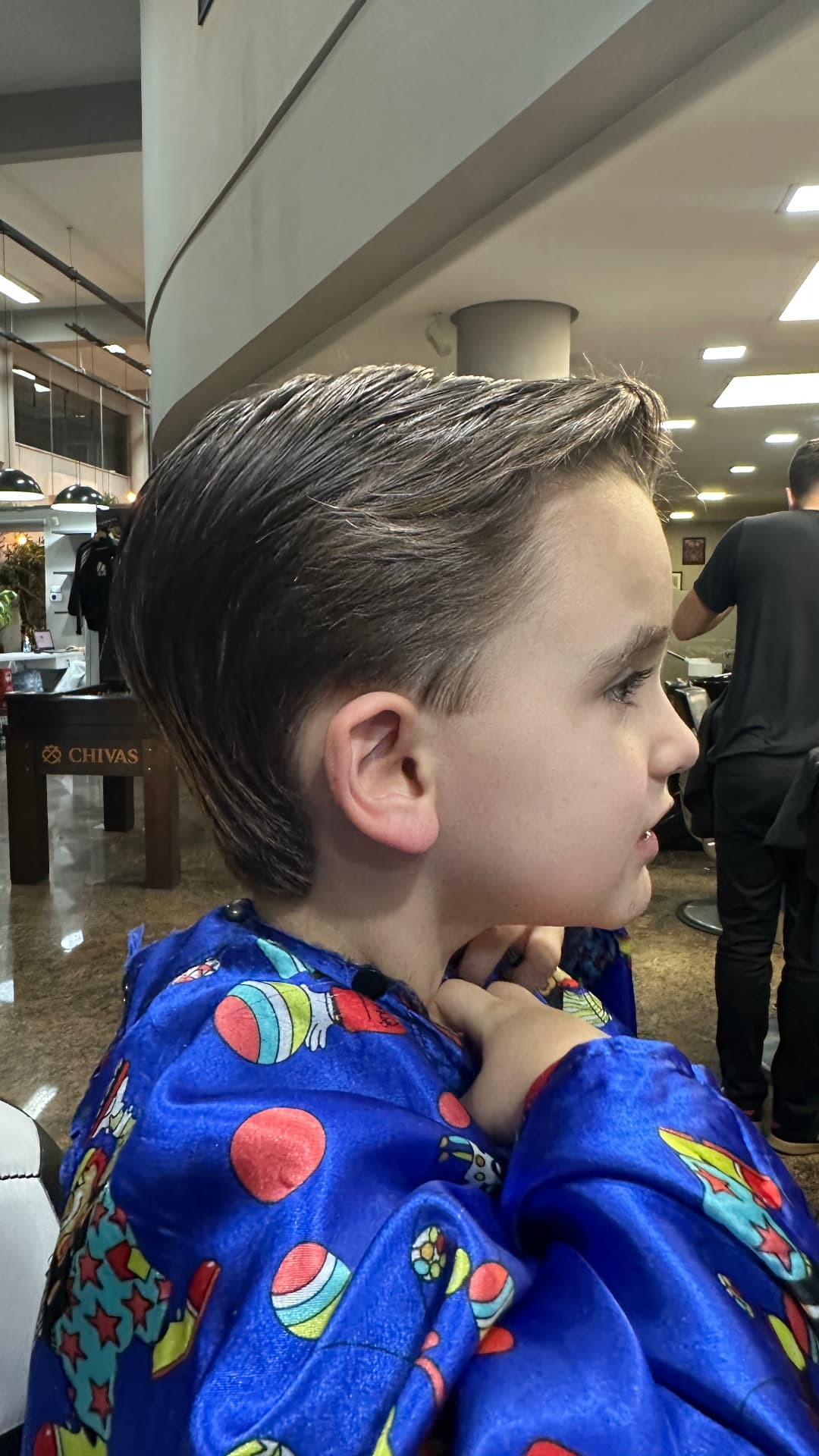 Corte infantil com laterais degradê e topo penteado para o lado, visto de perfil